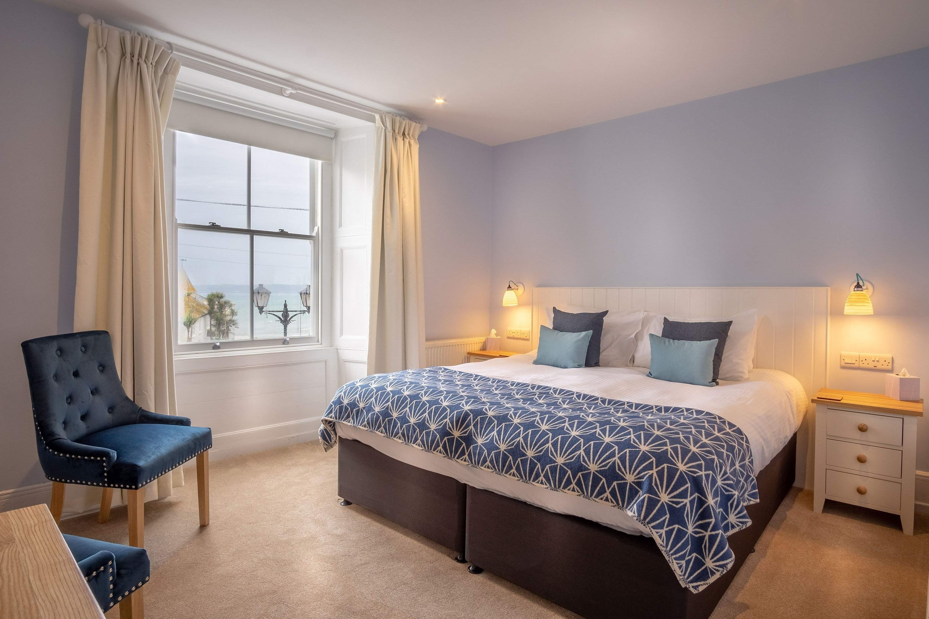 Een slaapkamer met een groot bed, een stoel, een nachtkastje en een raam met gordijnen.