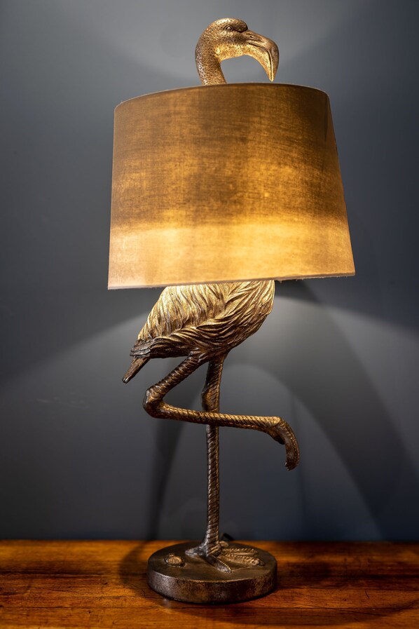 Una lámpara con diseño de pájaro sobre una mesa de madera contra un fondo oscuro.