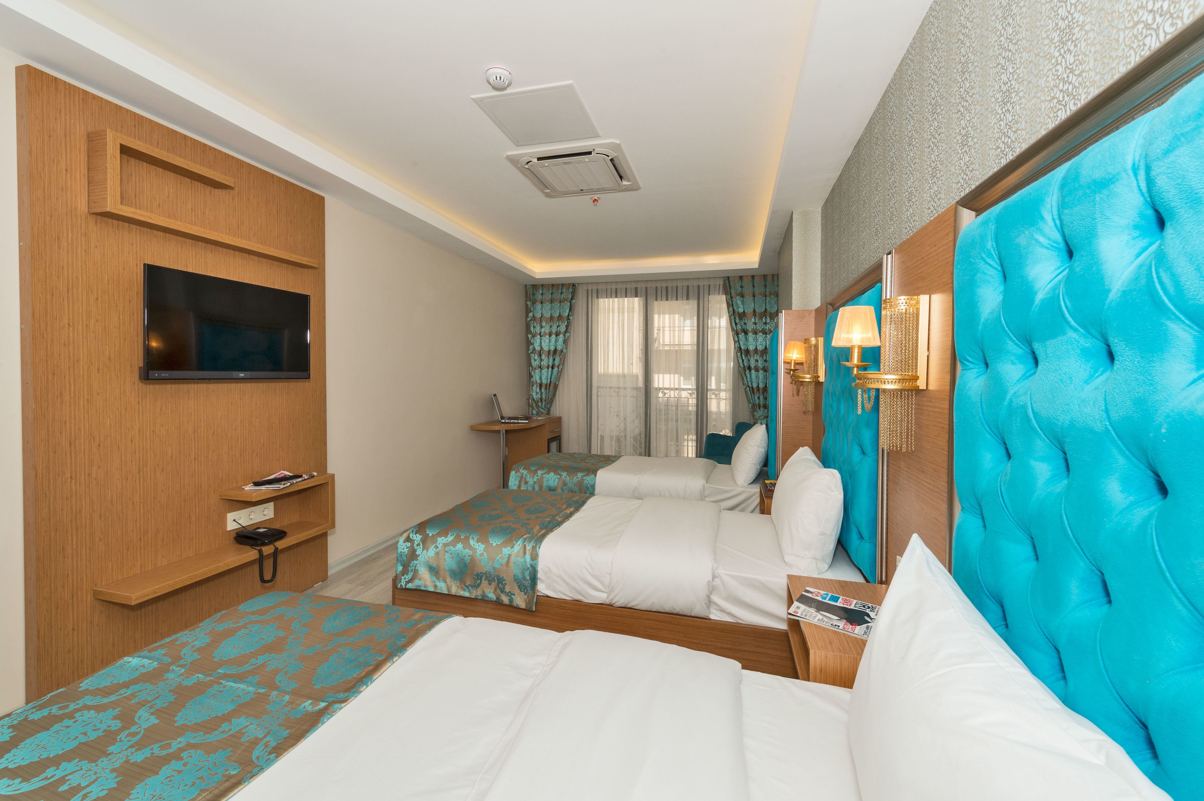 A hotel room with two beds, a TV, a bedside table, and a window with curtains.