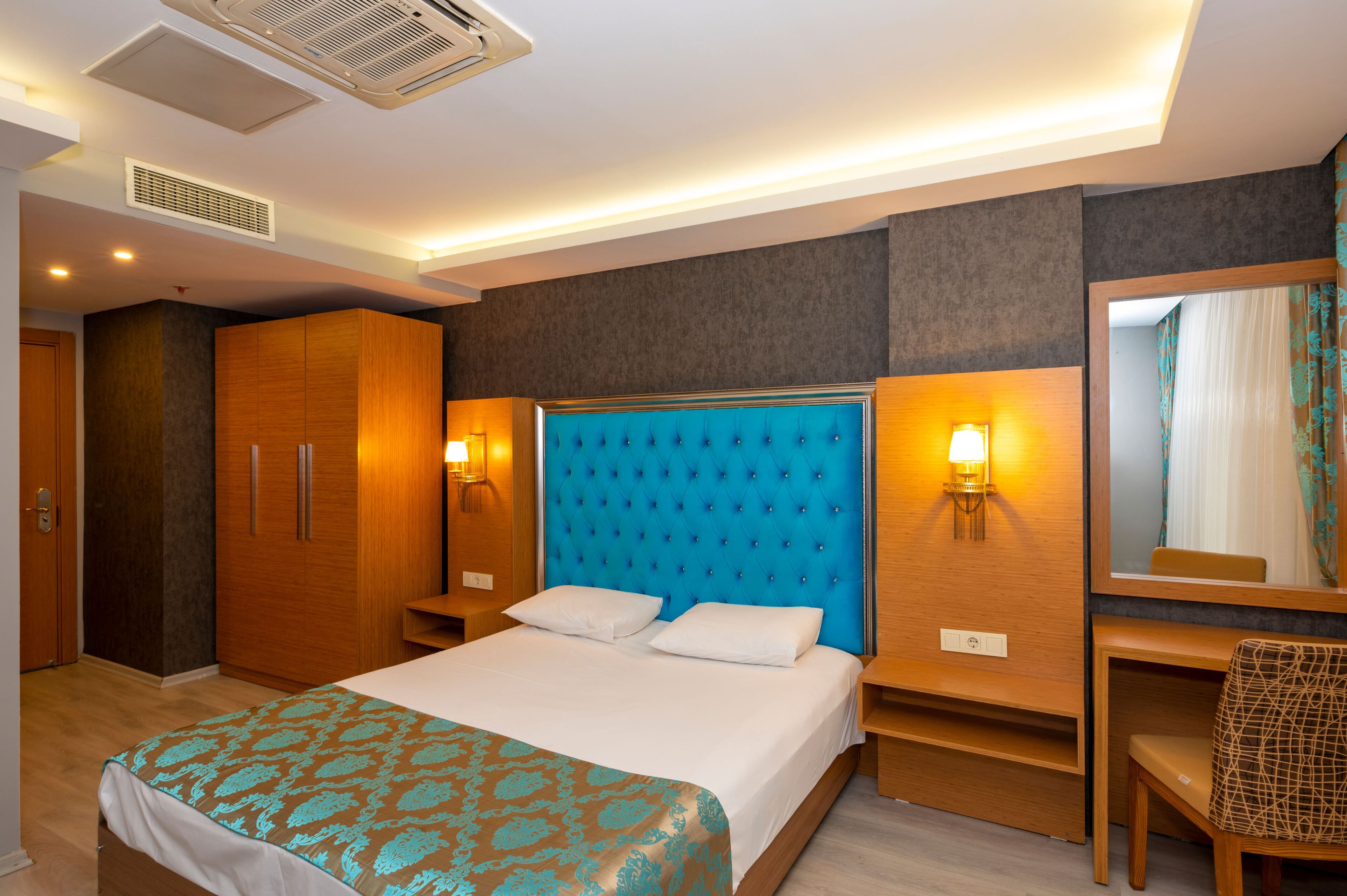A hotel room with a large bed, wooden wardrobe, bedside tables, and a mirror.