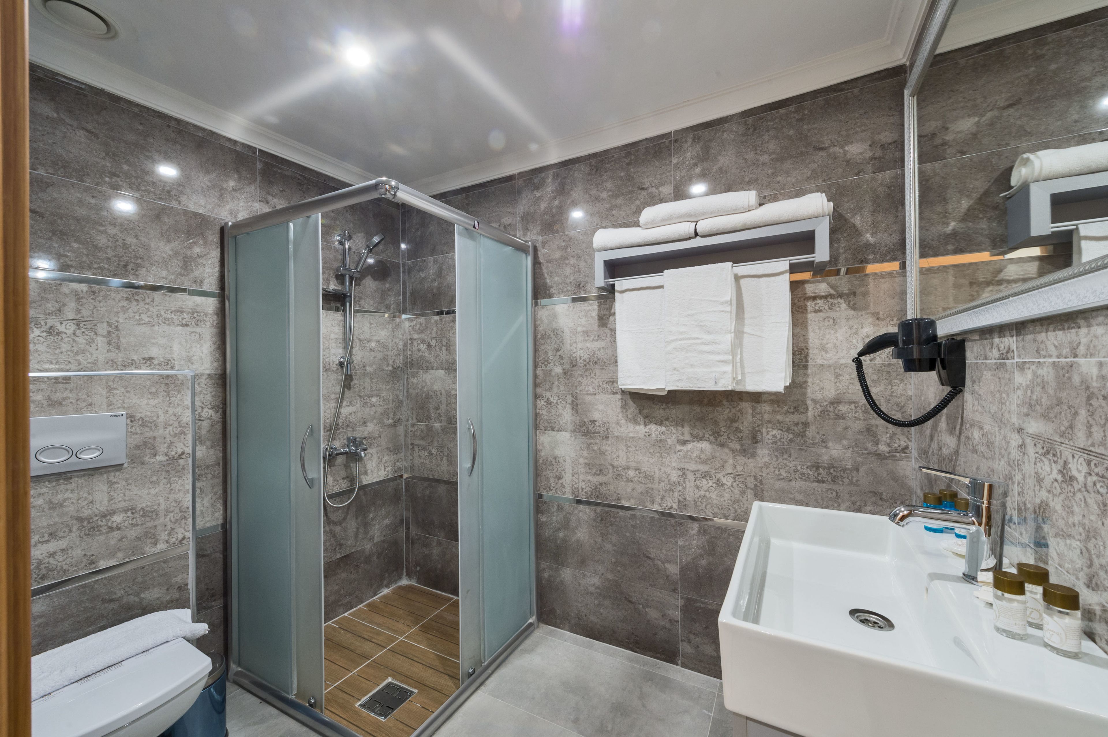 A modern bathroom with a glass-enclosed shower, a white sink, and a marble-tiled wall.