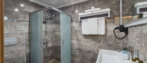 A modern bathroom with a glass-enclosed shower, a white sink, and a marble-tiled wall.