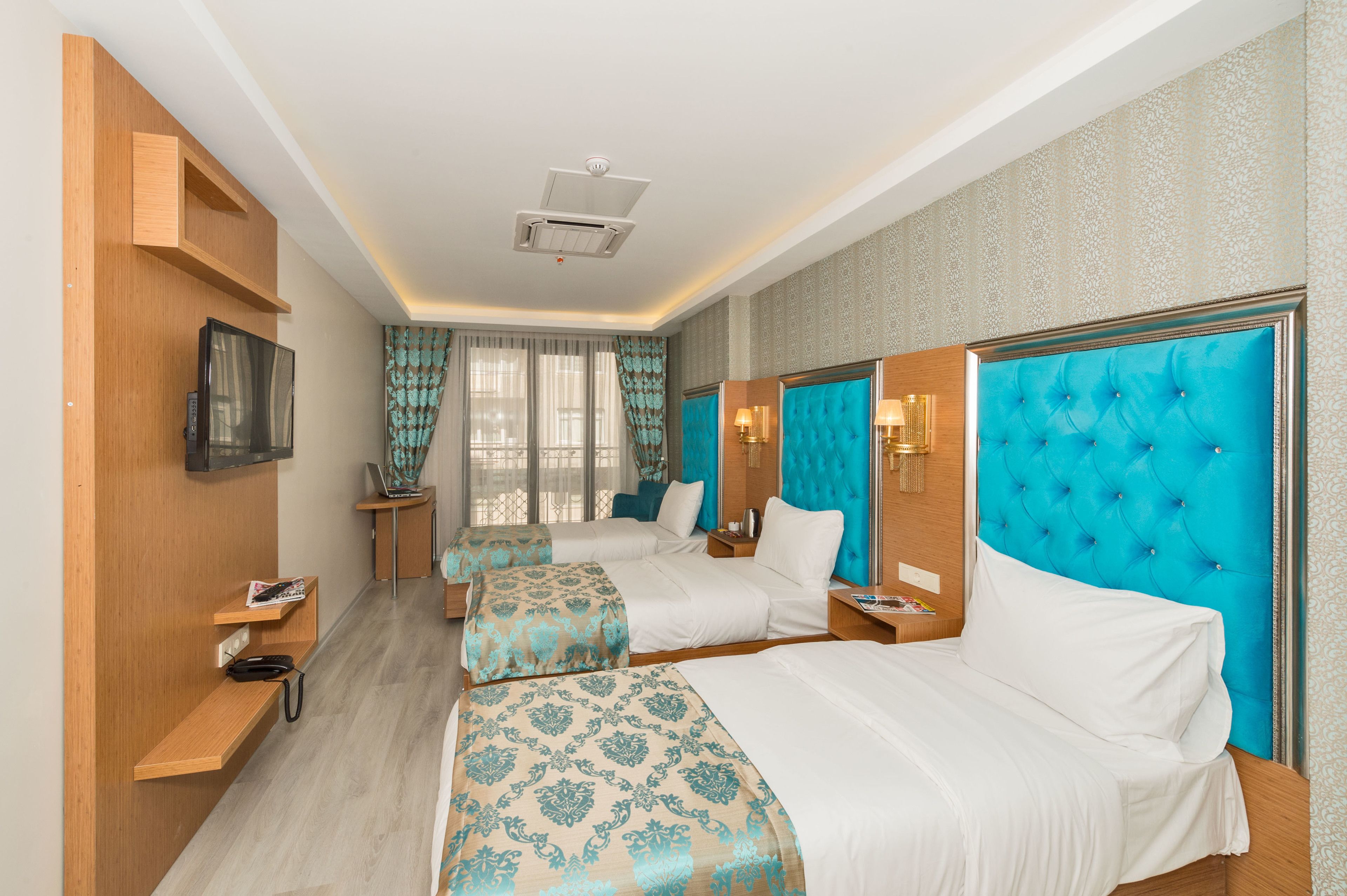 A hotel room with two beds, a TV mounted on the wall, and a small table with a lamp.