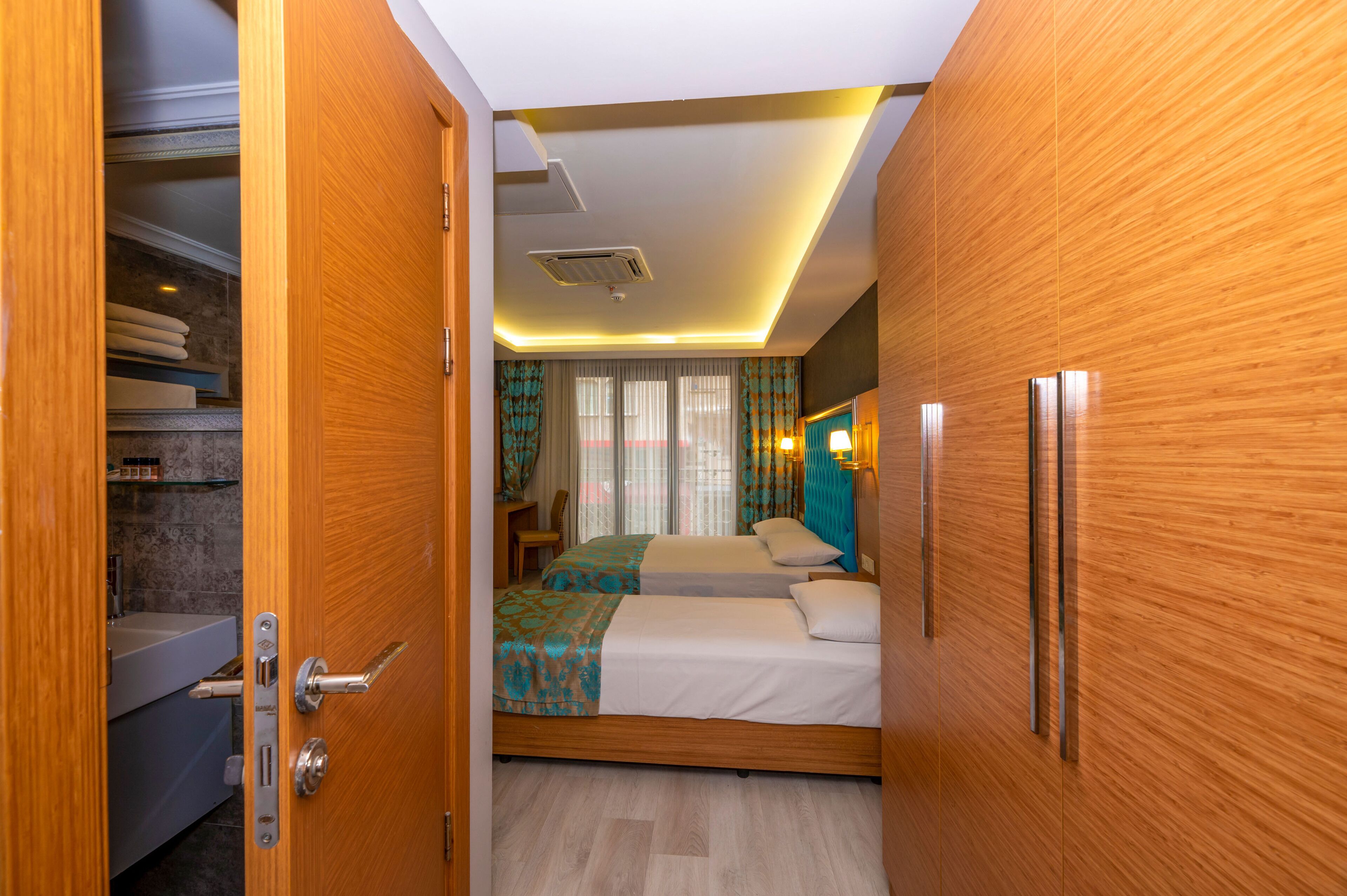 Una habitación de hotel con un armario de madera, una cama con colcha estampada, una mesita de noche y un baño con bañera e inodoro.