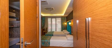 Una habitación de hotel con un armario de madera, una cama con colcha estampada, una mesita de noche y un baño con bañera e inodoro.