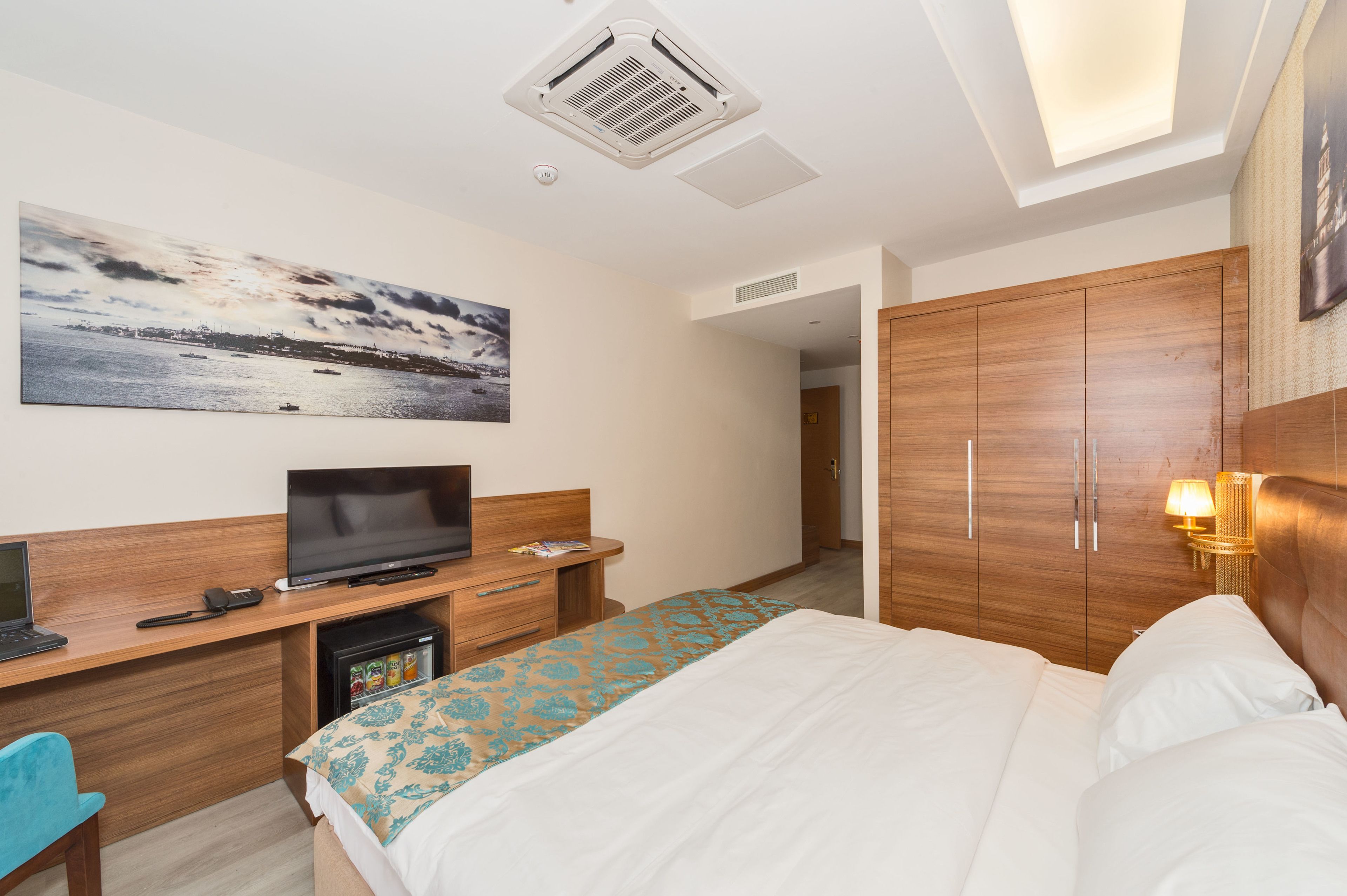 Ein Hotelzimmer mit einem Bett, einem Schreibtisch mit Computer, einem Fernseher und einem kleinen Kühlschrank.
