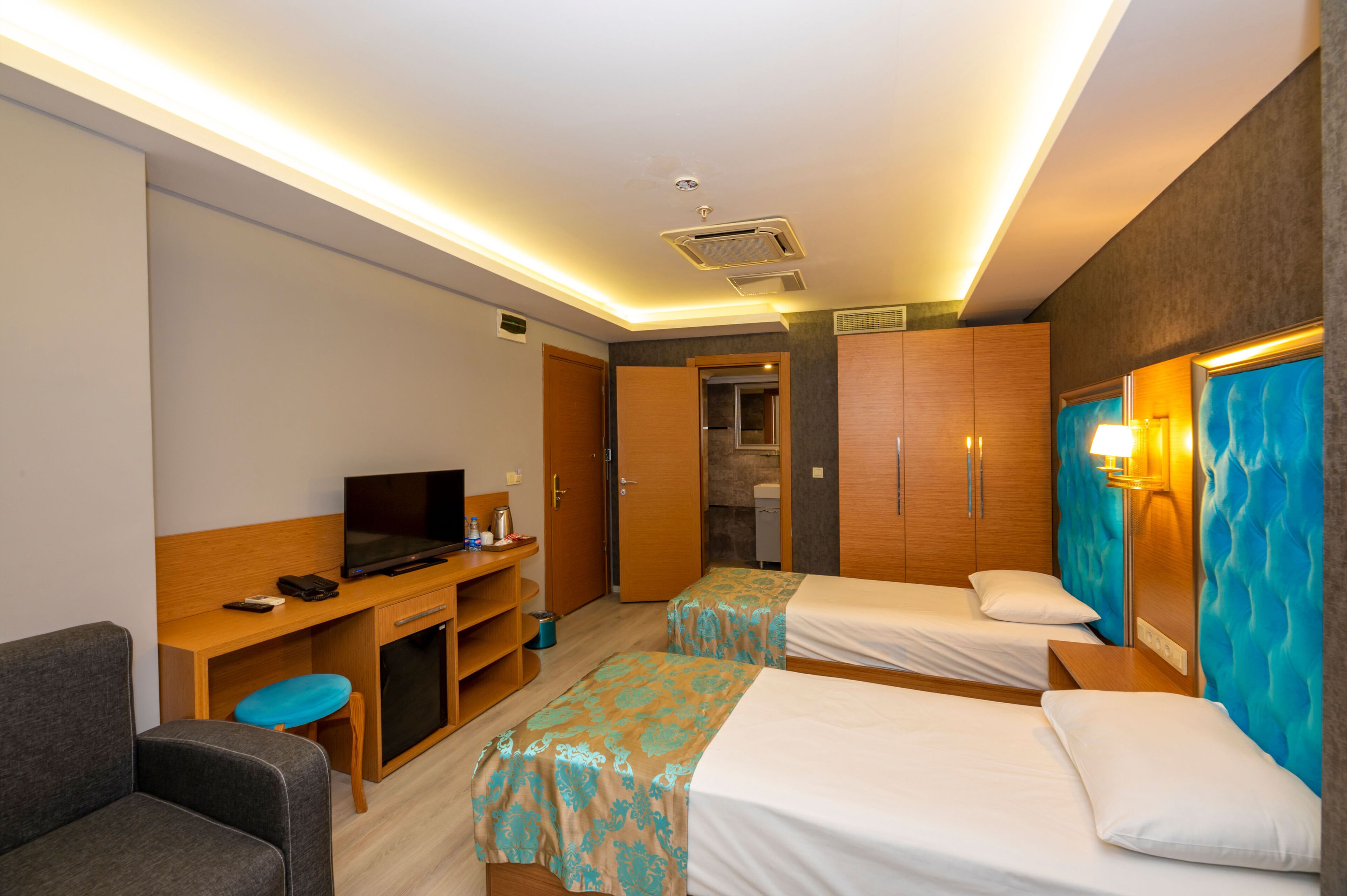 A hotel room with two beds, a desk with a TV, a chair, and a bathroom door.