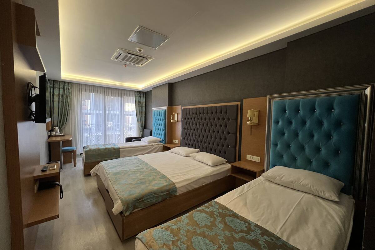 A hotel room with two beds, a desk, a TV, and a window with curtains.