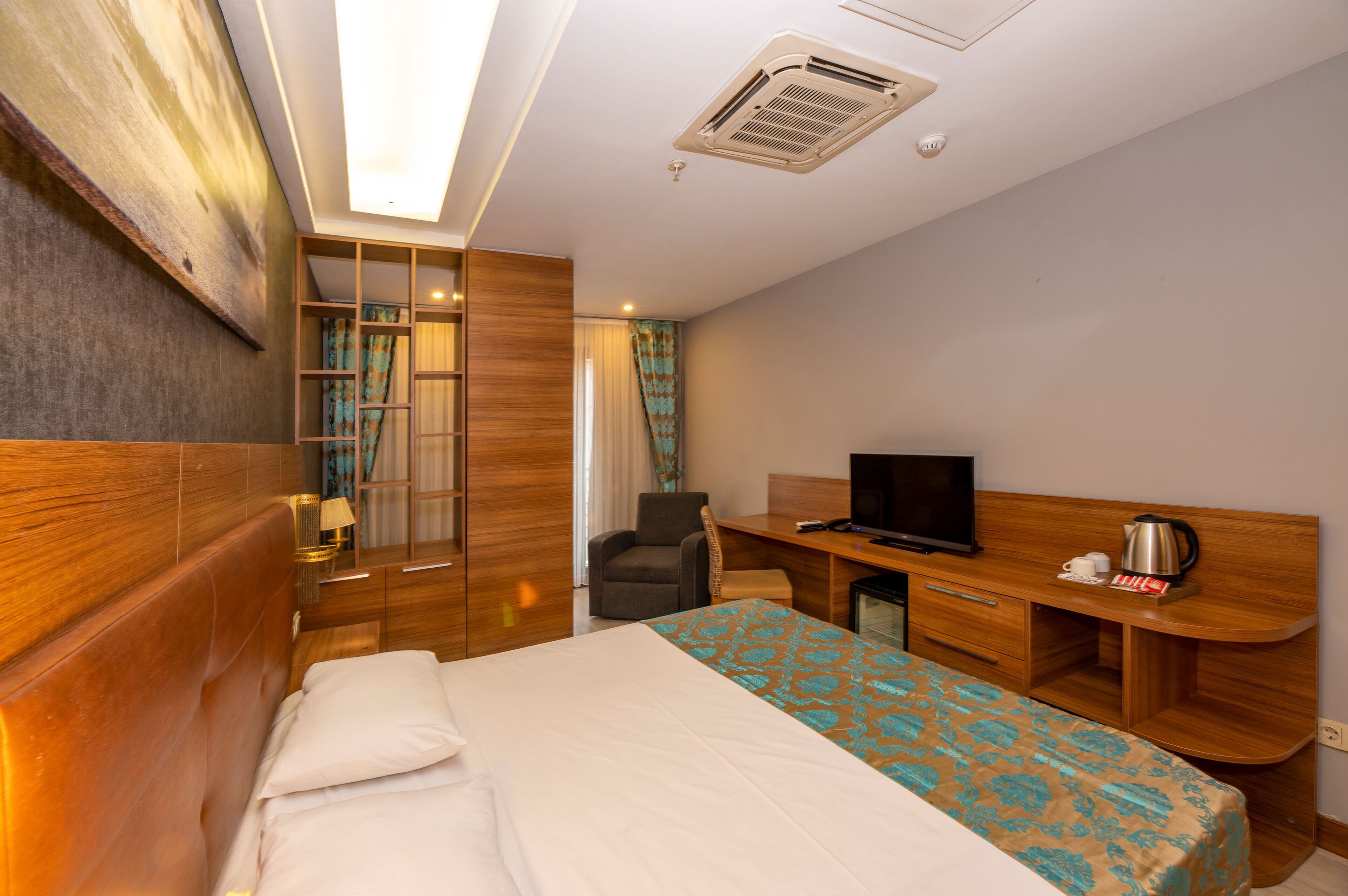 A hotel room with a bed, a desk with a TV, a chair, a desk lamp, and a window with curtains.