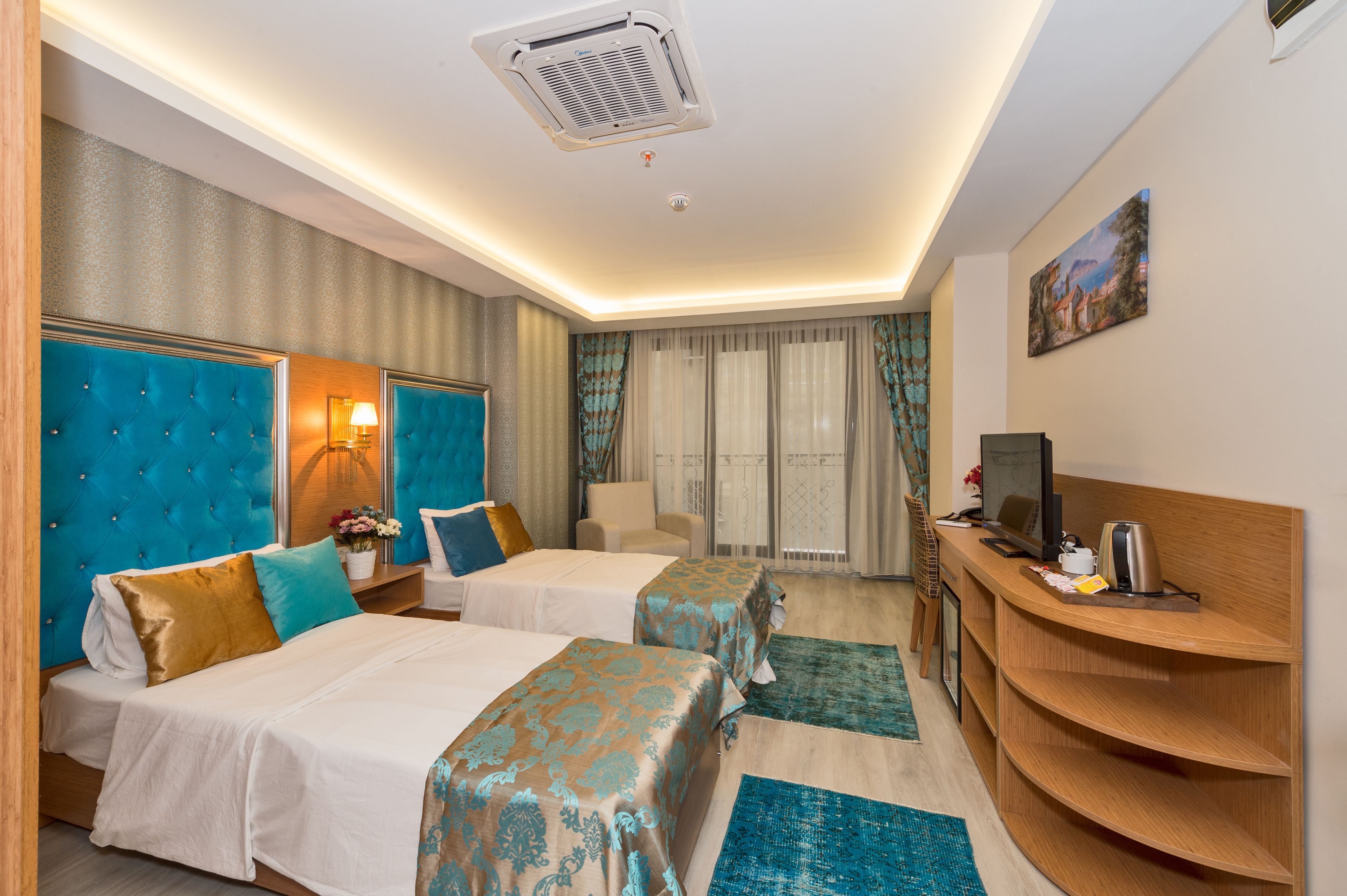 A hotel room with two beds, a desk, a TV, and a window with curtains.