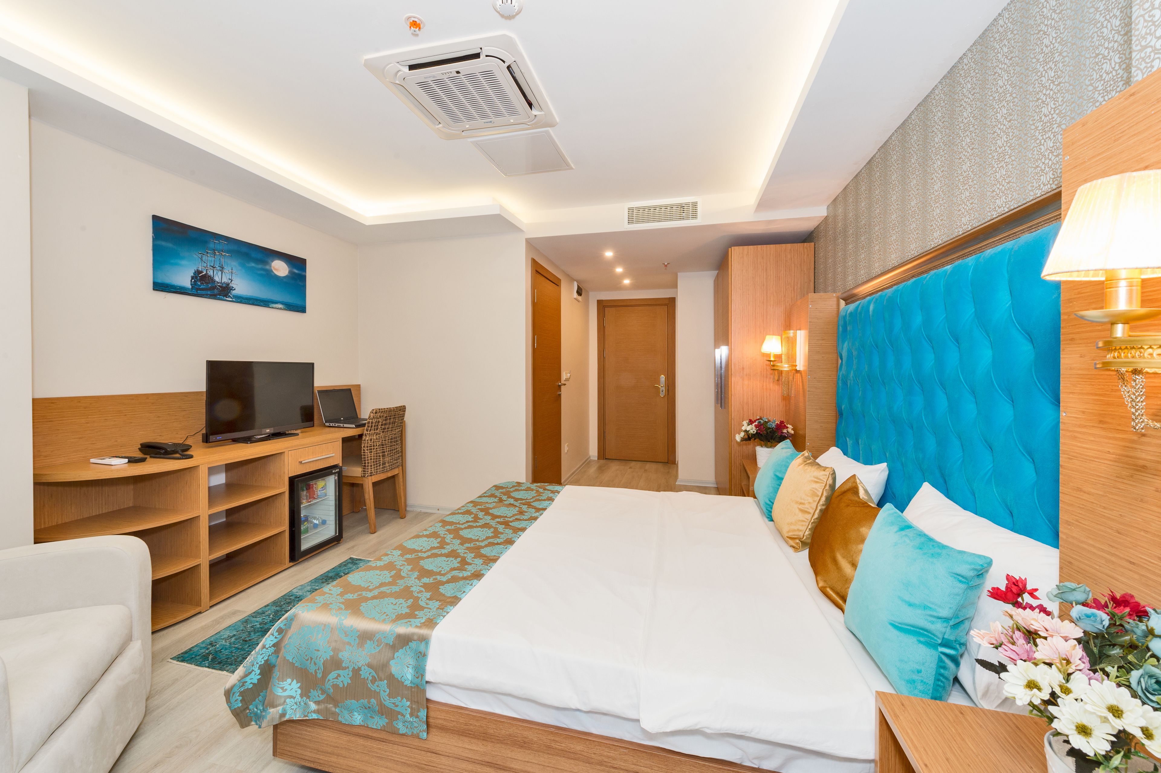A hotel room with a bed, a desk with a computer, a television, and a small refrigerator.