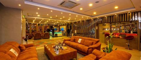 Um saguão de hotel com várias áreas de estar, uma recepção e um bar.