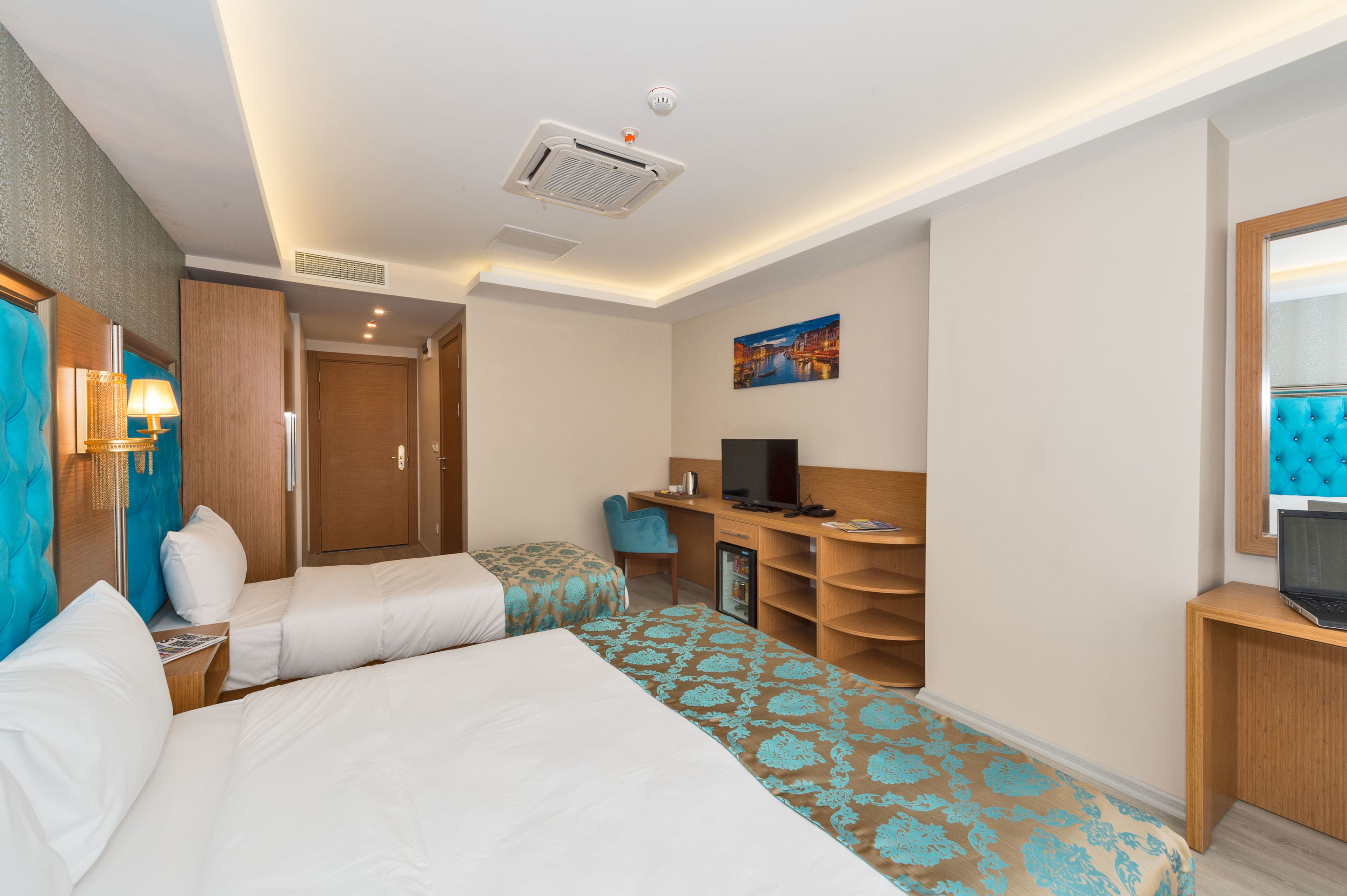 A hotel room with two beds, a desk, a television, and a small refrigerator.