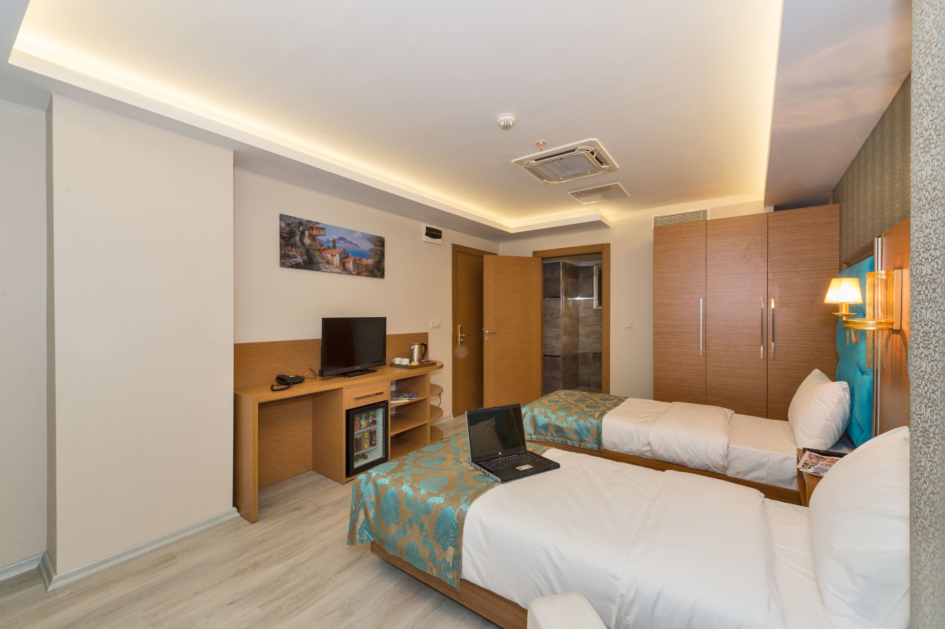 A hotel room with two beds, a desk with a laptop, a television, and a minibar.
