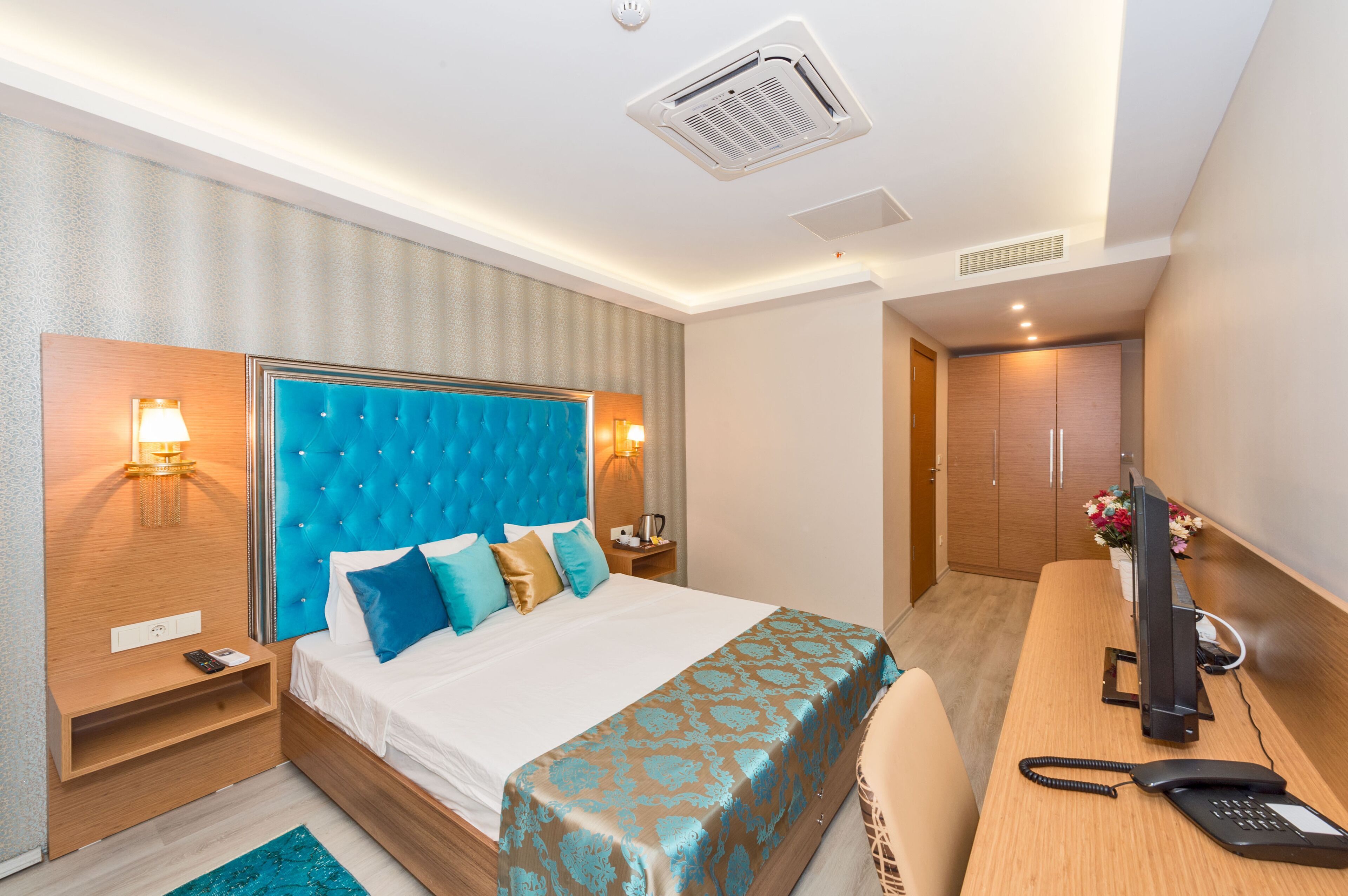 A hotel room with a large bed, bedside tables, a desk with a telephone, and a television.