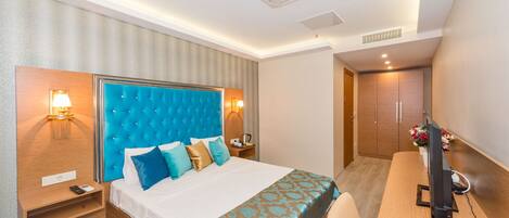 A hotel room with a large bed, bedside tables, a desk with a telephone, and a television.
