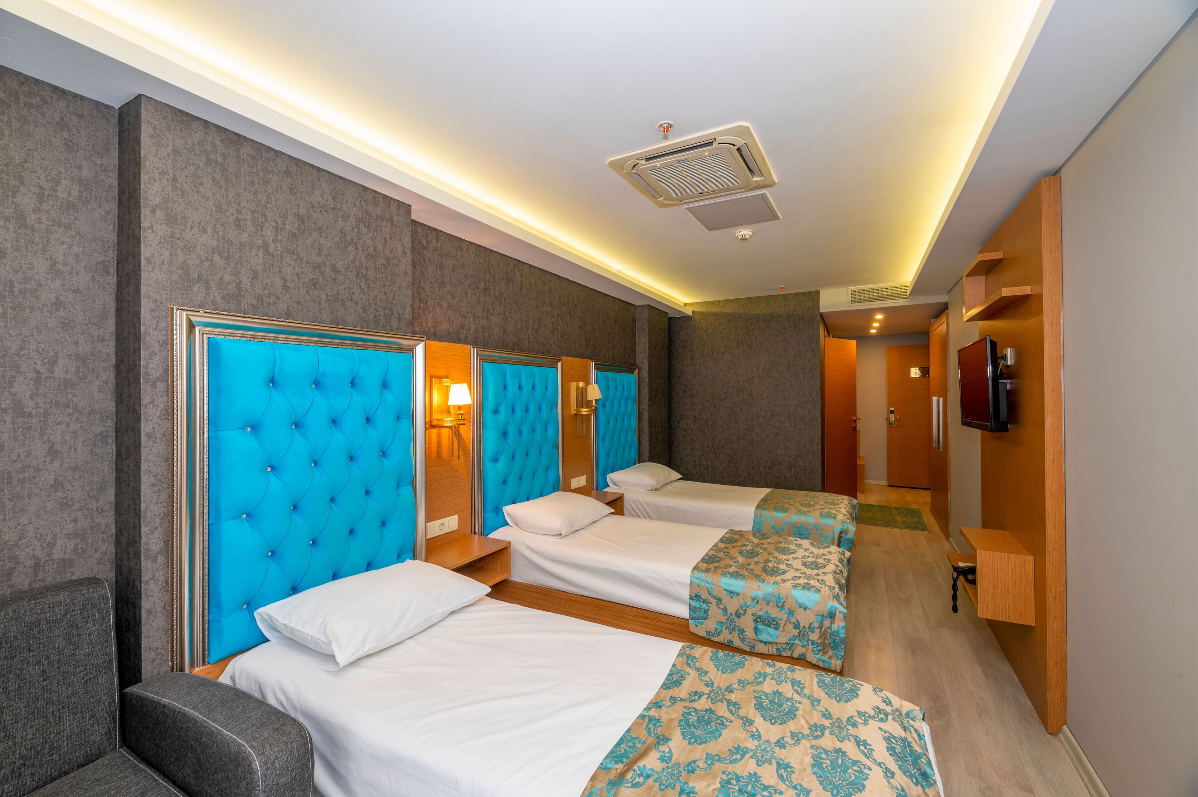 A hotel room with three beds, a television, and a bathroom visible in the background.