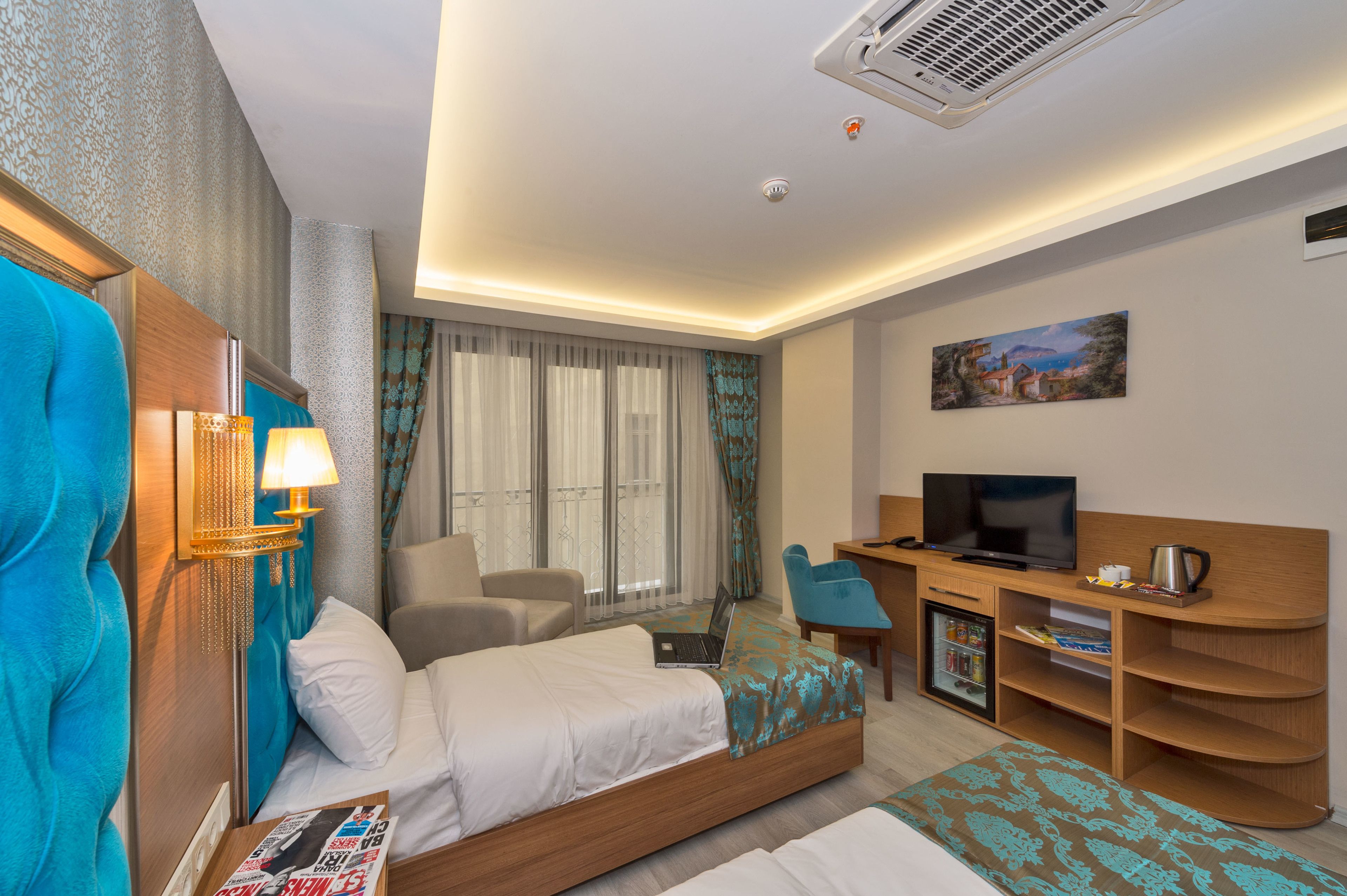 A hotel room with a bed, a desk with a television, a coffee maker, and a small refrigerator.