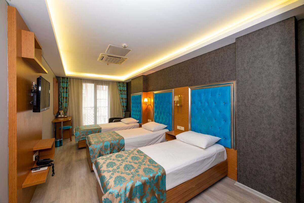 A hotel room with two beds, a desk, a TV, and a window with curtains.