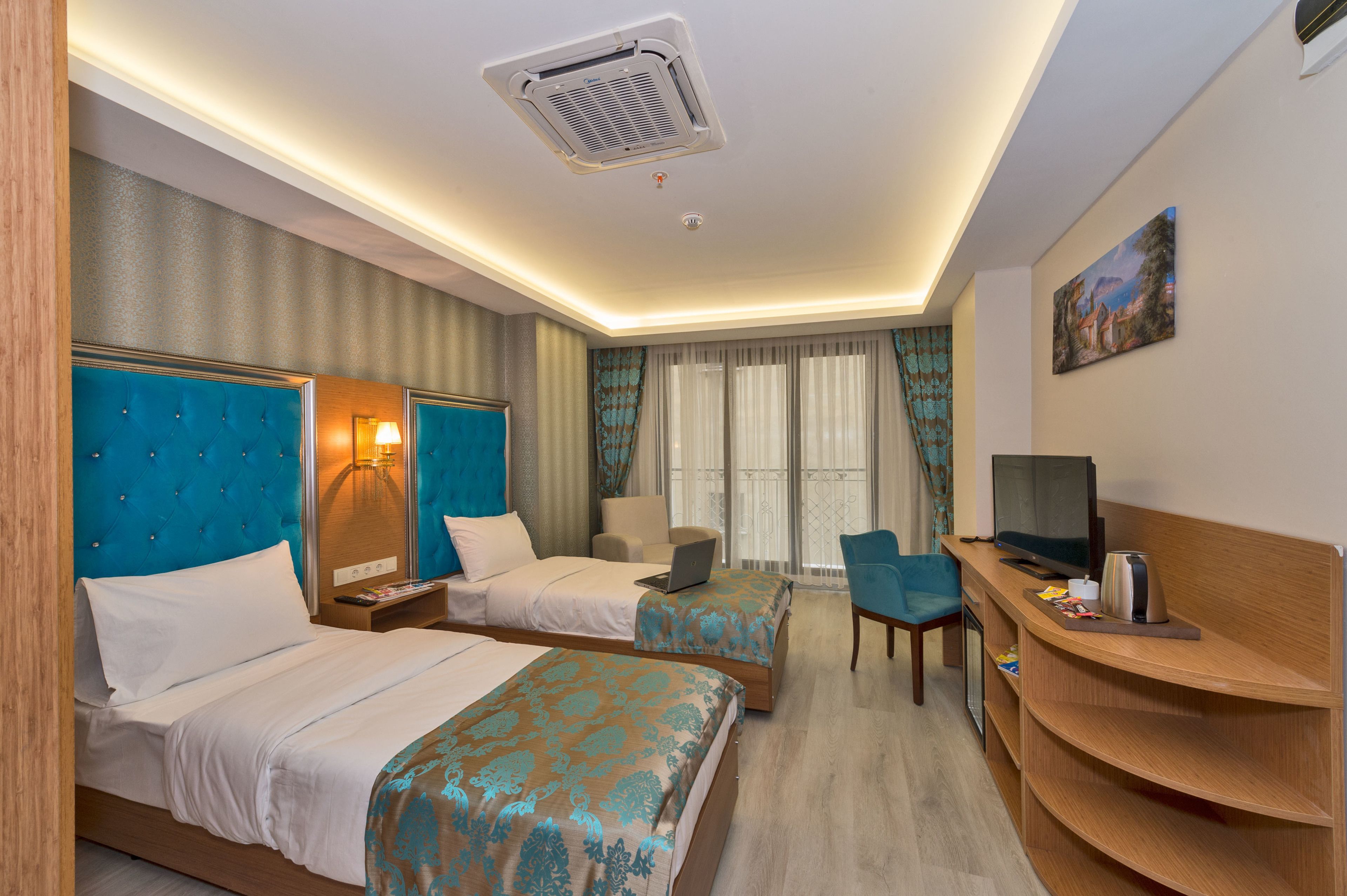 A hotel room with two beds, a desk with a TV, a laptop, and a chair.
