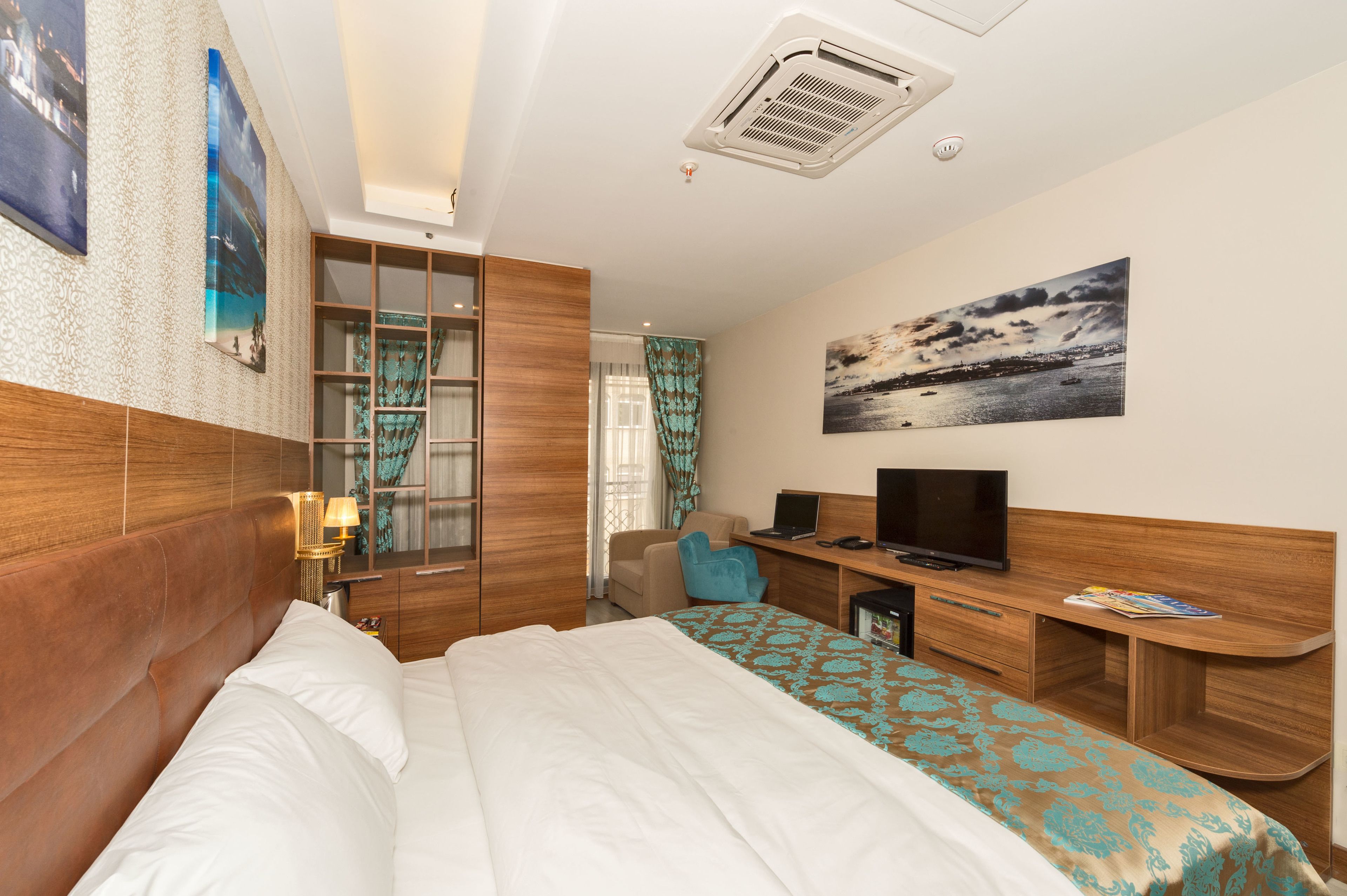 A hotel room with a bed, a desk, a television, and a large window with curtains.