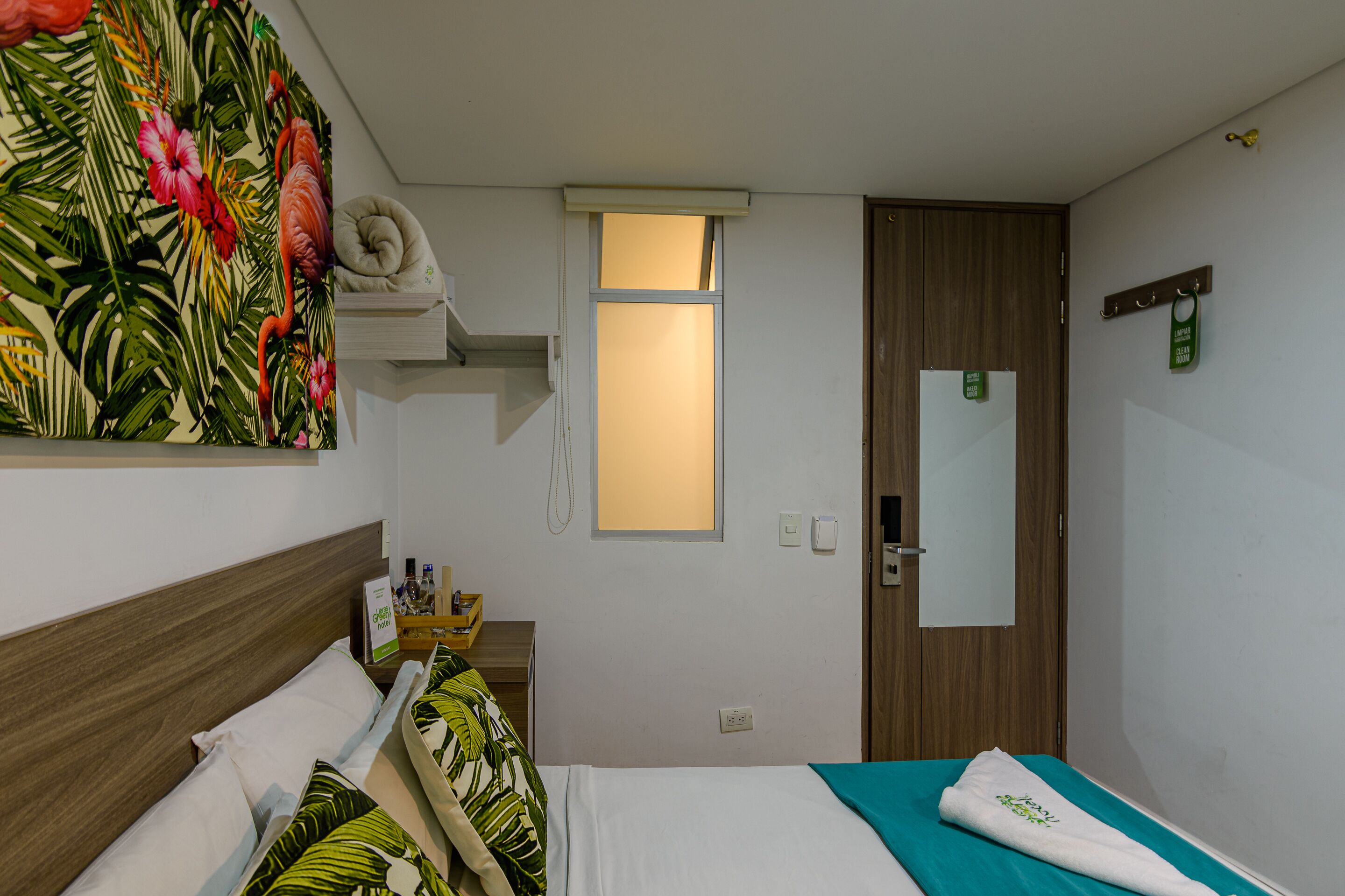 Habitación de hotel con cama, ventana, puerta y pared decorada con un mural tropical.