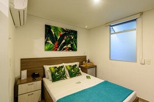 Habitación de hotel con cama, mesita de noche, una pequeña mesa, un cuadro y una ventana.