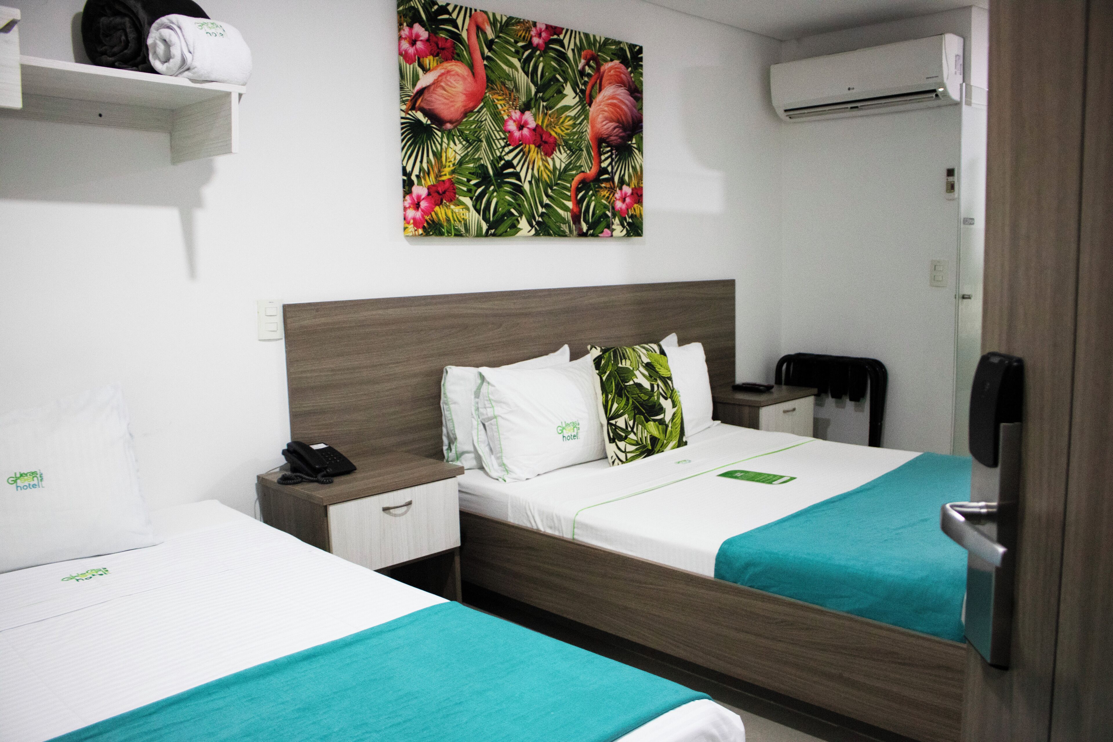 Habitación de hotel con dos camas, un cuadro de flamencos, un equipo de aire acondicionado y un teléfono en la mesita de noche.