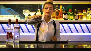 En bartender laver en drink bag en bar med forskellige flasker alkohol og et ur i baggrunden.