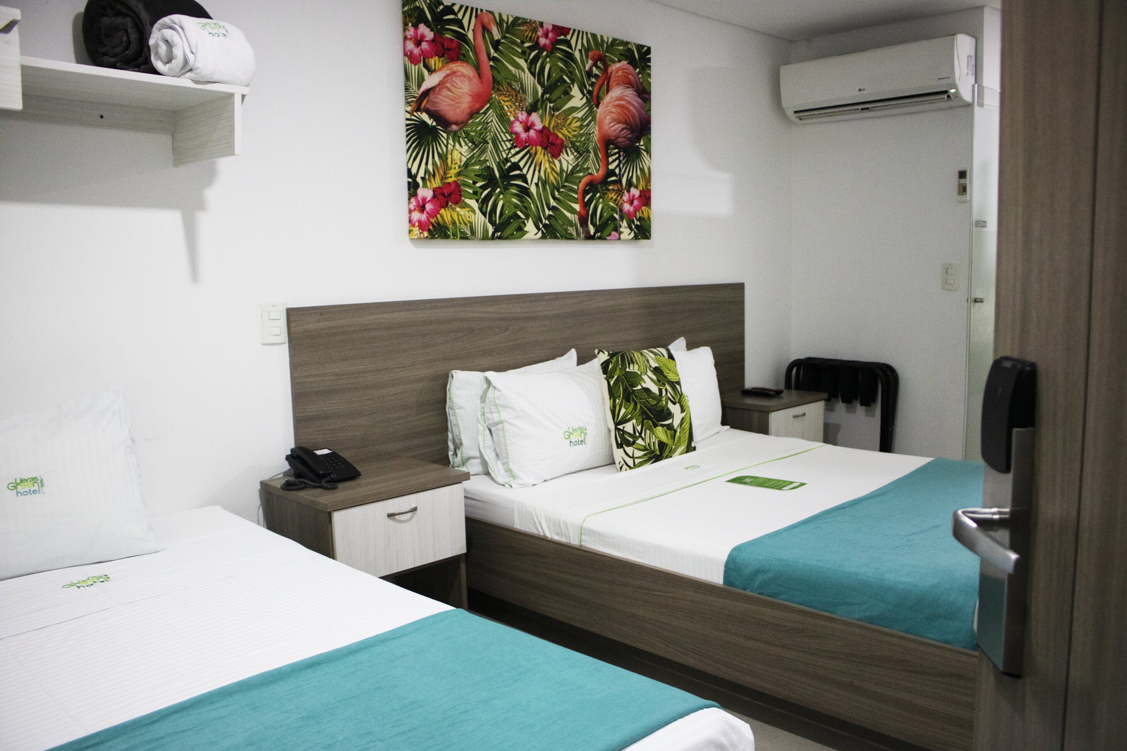 A hotel room with two beds, a wooden headboard, a painting of flamingos, a telephone, and a minibar.