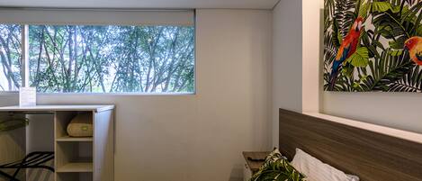 A bedroom with a bed, a desk, and a window with a view of trees.