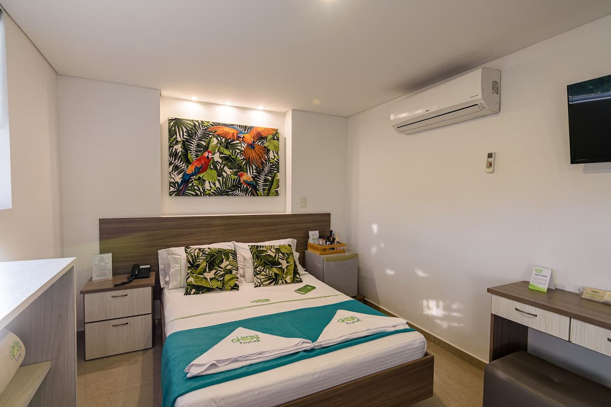 Une chambre d’hôtel équipée d’un lit, d’un bureau, d’une table de chevet, d’un climatiseur et d’un téléviseur fixé au mur.