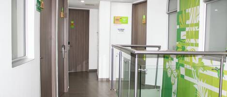 A modern hotel corridor with glass railings, a green wall with a leaf pattern, and signs indicating room availability.