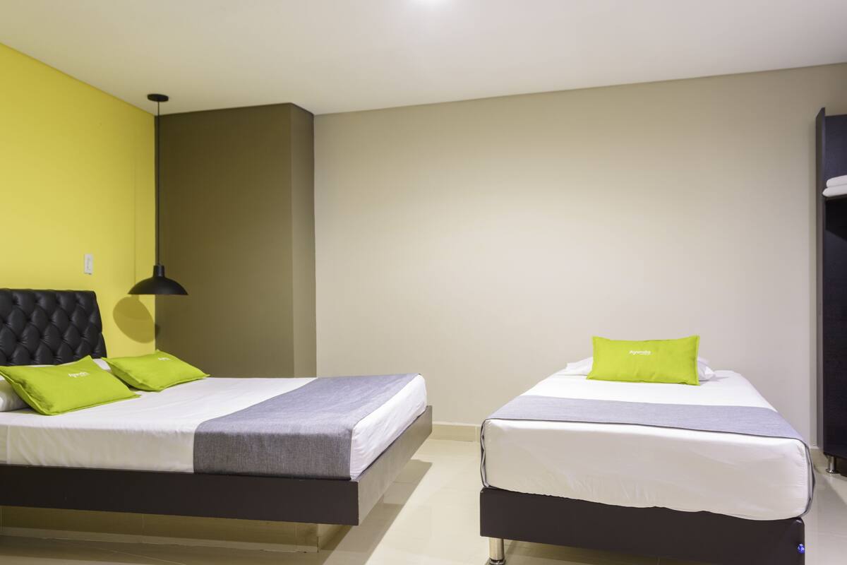 Two single beds with grey and white bedding, green pillows, and a black headboard.