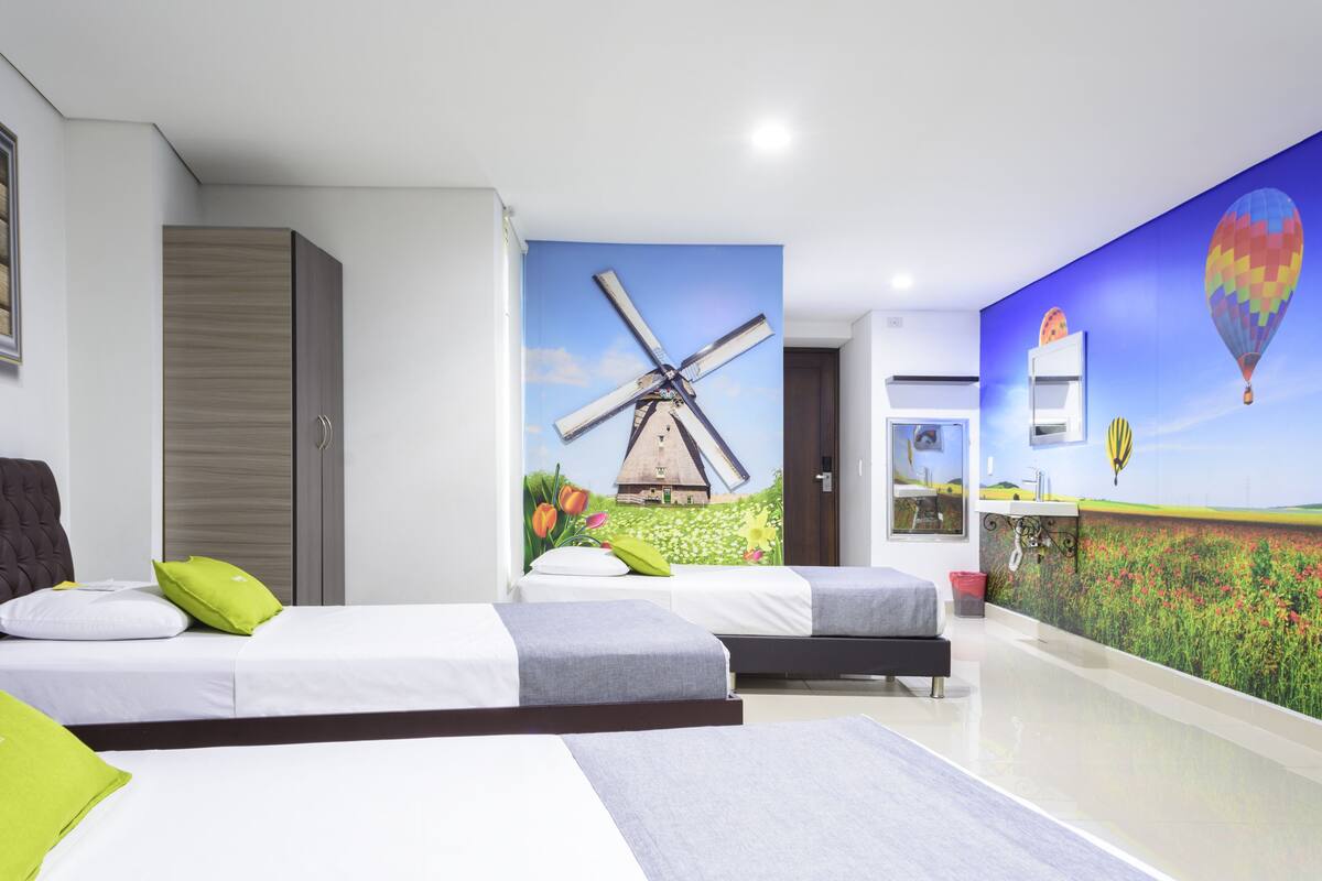 A hotel room with two beds, a wardrobe, a wall mural of a windmill, and a hot air balloon.