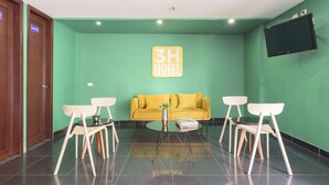 A hotel lobby with a green wall, a yellow sofa, and a TV mounted on the wall. - 3H Hotel Centro Histórico (Medellín)