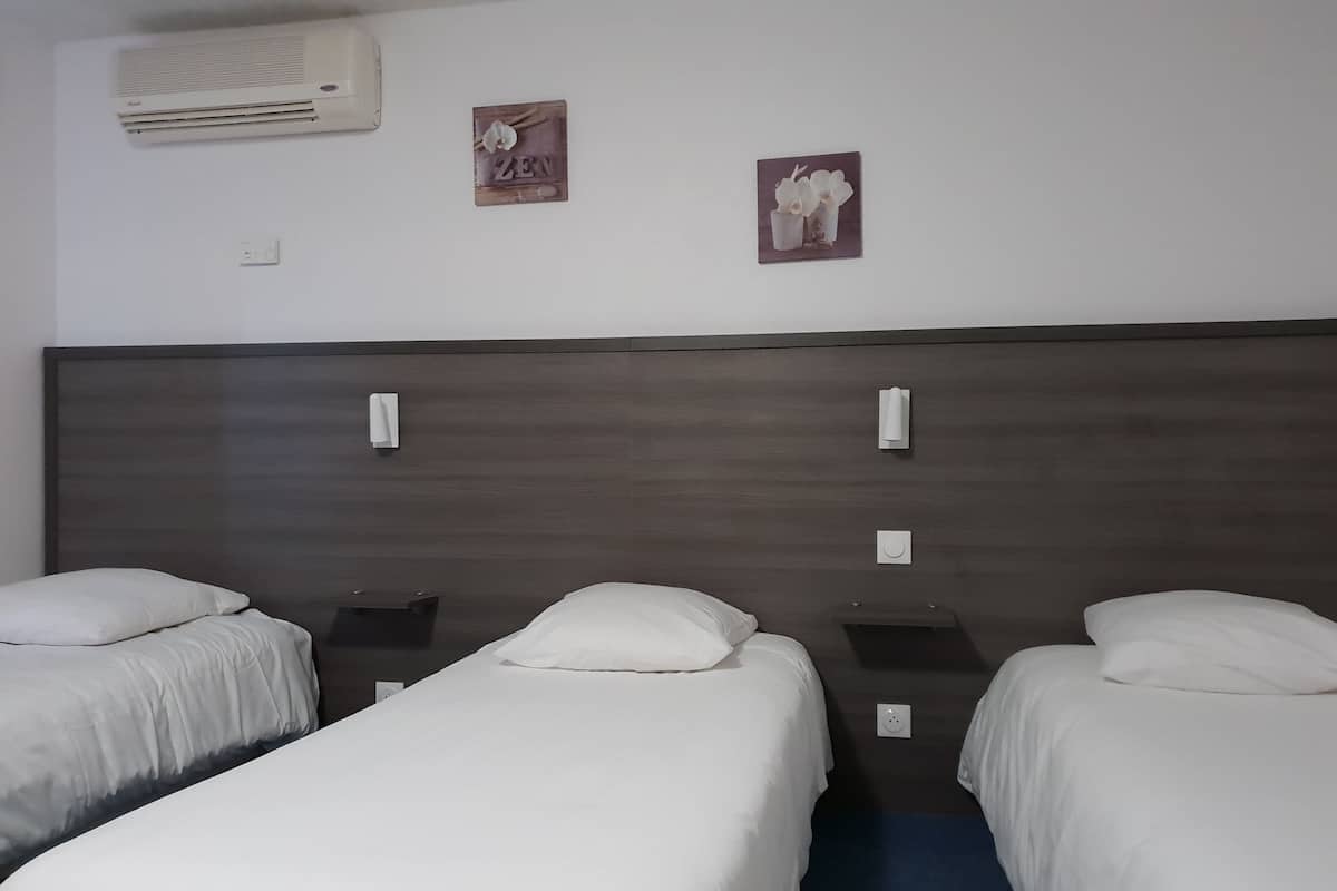 Une chambre d’hôtel avec deux lits simples, une tête de lit en bois foncé, deux climatiseurs fixés au mur et deux petits tableaux encadrés.