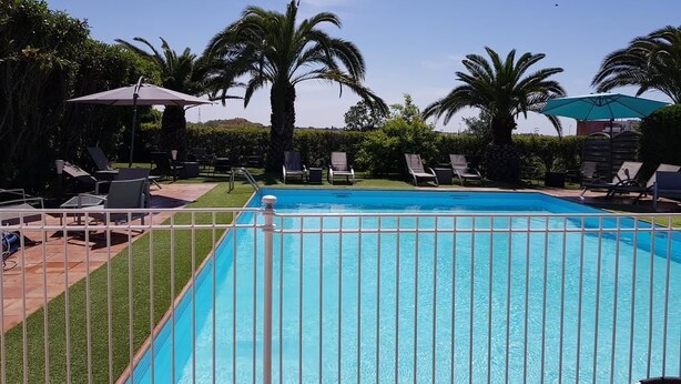 A swimming pool with a white fence, surrounded by palm trees and lounge chairs. - Hotel Althea (Béziers)