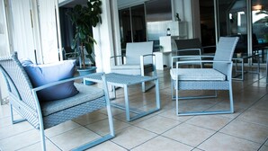 A modern outdoor seating area with wicker chairs and a table, large windows, and a potted plant. - Hotel Althea (Béziers)