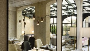 Comedor con mesas y sillas, una araña y vistas a través de amplias ventanas.