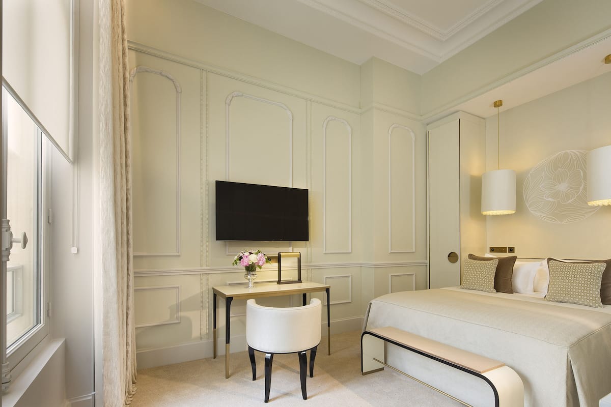 Habitación de hotel con cama, escritorio, silla, televisión y lámpara fijada a la pared.