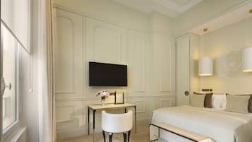 Quarto de hotel com cama, escrivaninha, cadeira, televisão e luminária na parede.