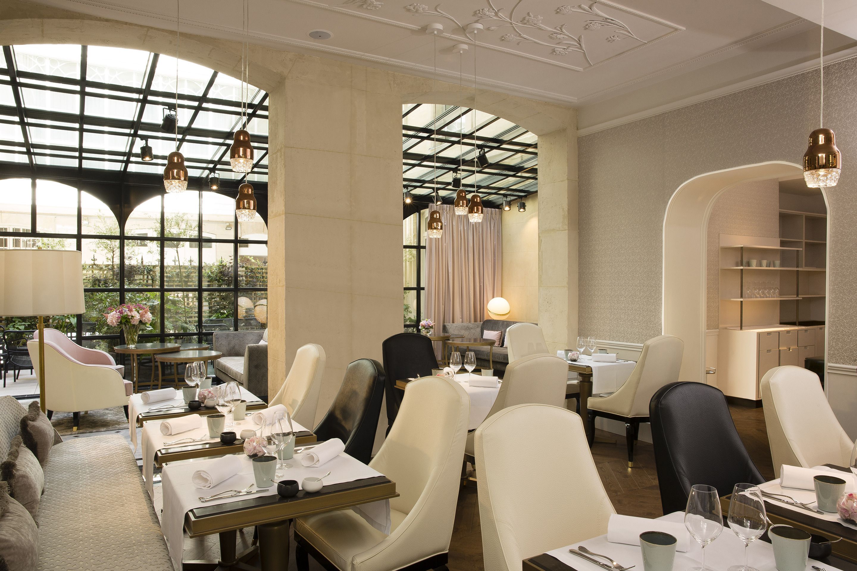Un restaurant avec de hauts plafonds, de grandes fenêtres et des lustres modernes. Les tables sont dressées avec des nappes blanches et de beaux couverts.