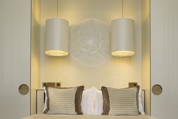 A modern hotel room with a large bed, two wall-mounted lamps, and a decorative wall panel. - Hotel Le Narcisse Blanc & Spa (Paris)
