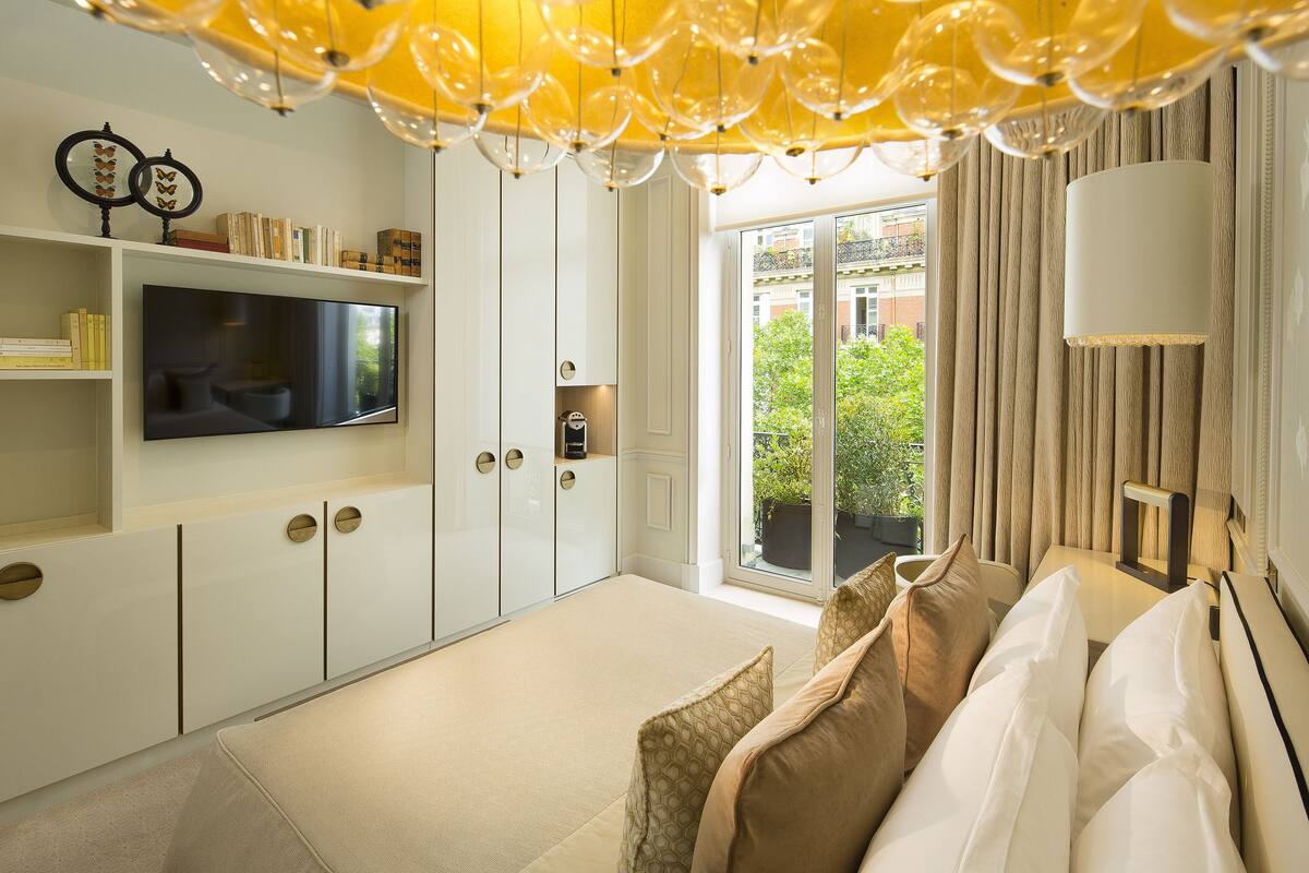 Habitación de hotel moderna con una gran televisión de pantalla plana, un sofá con cojines estampados y vistas a zonas verdes por la ventana.