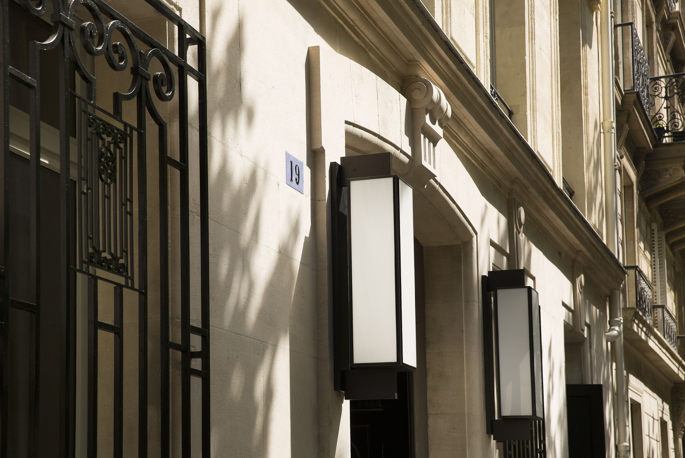 A building facade with a wrought iron gate, a street lamp, and a number sign indicating the address.