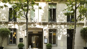 A building facade with a symmetrical design, featuring a central entrance with a glass door, potted plants on either side, and a sign above the door. - Hotel Le Narcisse Blanc & Spa (Paris)
