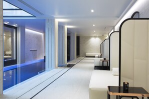 Un moderno espacio de spa con un jacuzzi de vidrio, zonas de estar y un mostrador de recepción.
