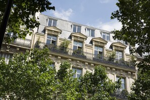 Un edificio de varios pisos con un estilo arquitectónico clásico, que cuenta con balcones con barandillas de hierro forjado y grandes ventanales.