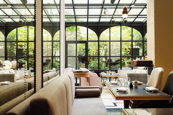 Un restaurante con techos altos, amplias ventanas y diversas opciones de asientos, incluyendo cabinas y mesas.